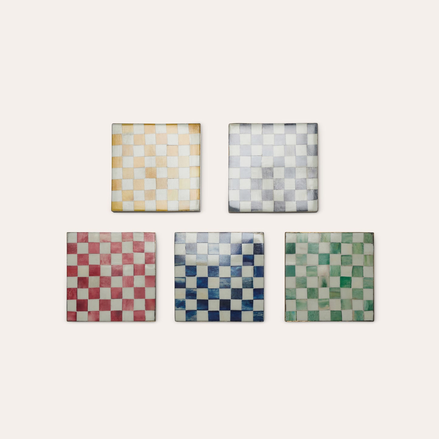 Five square drink coaster tiles with checkered patterns in yellow, grey, red, blue and green colours on a light background.