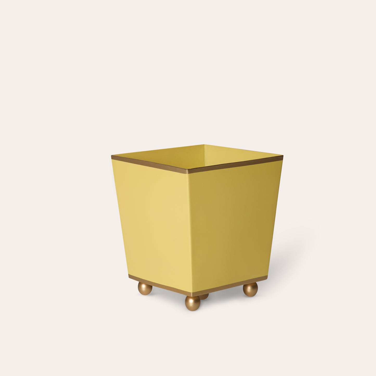 Yellow metal waste paper basket with gold ball feet on a white background