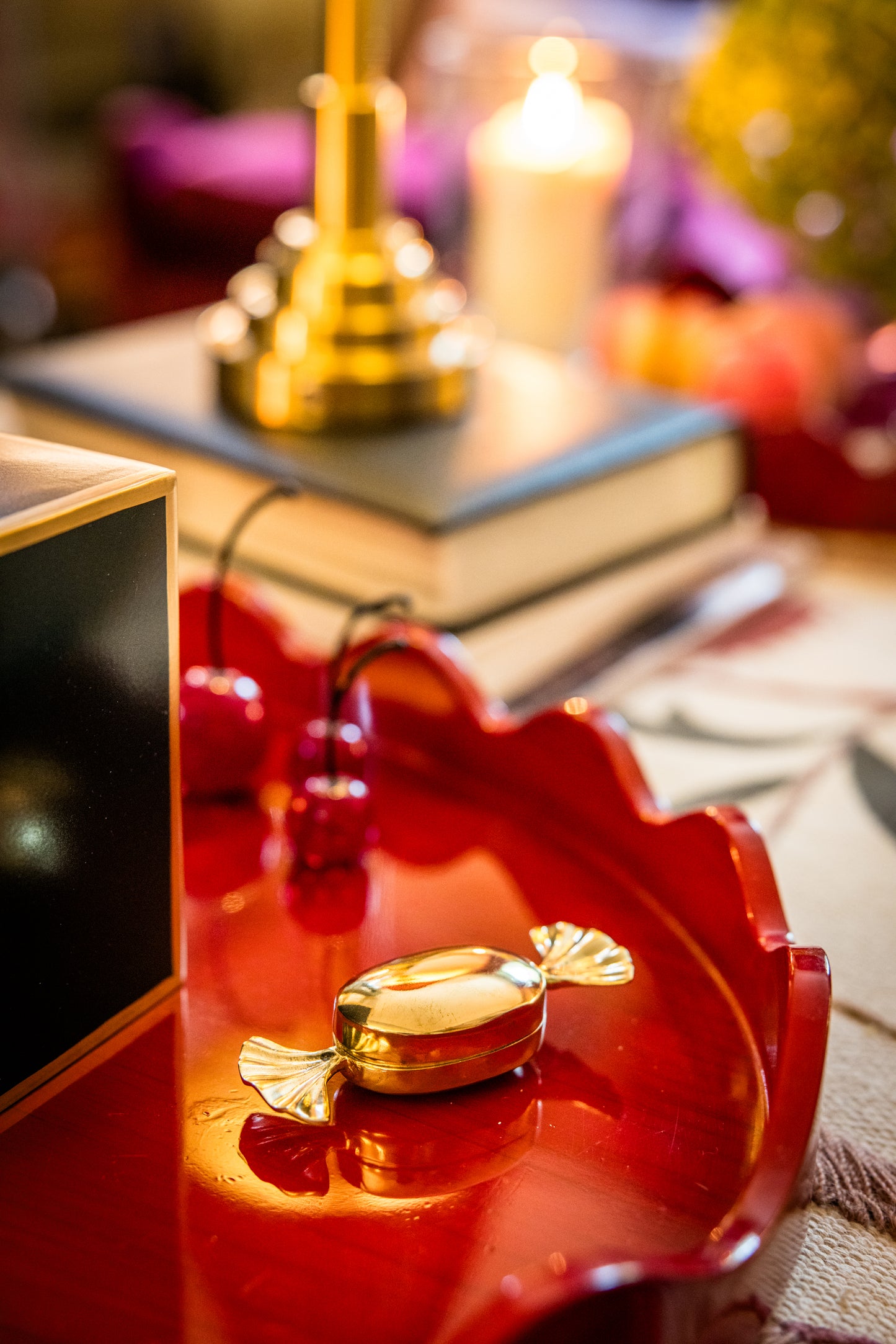 Decorative red tray with wiggle edge trim on a fabric with books and lamps in the background. A small gold candy shaped container on it in the foreground.