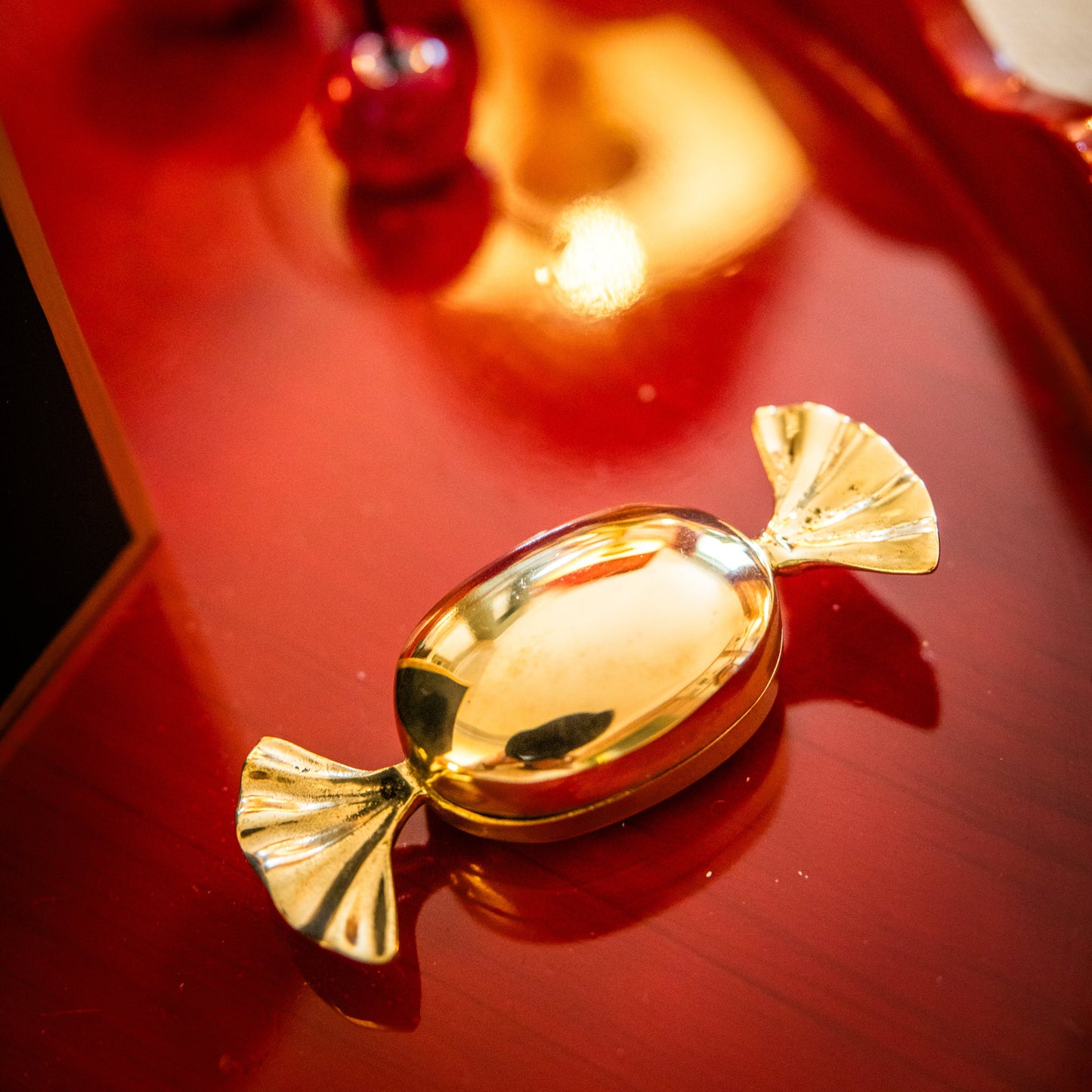 Gold reflective candy-shaped decorative homeware accessory on a red surface.