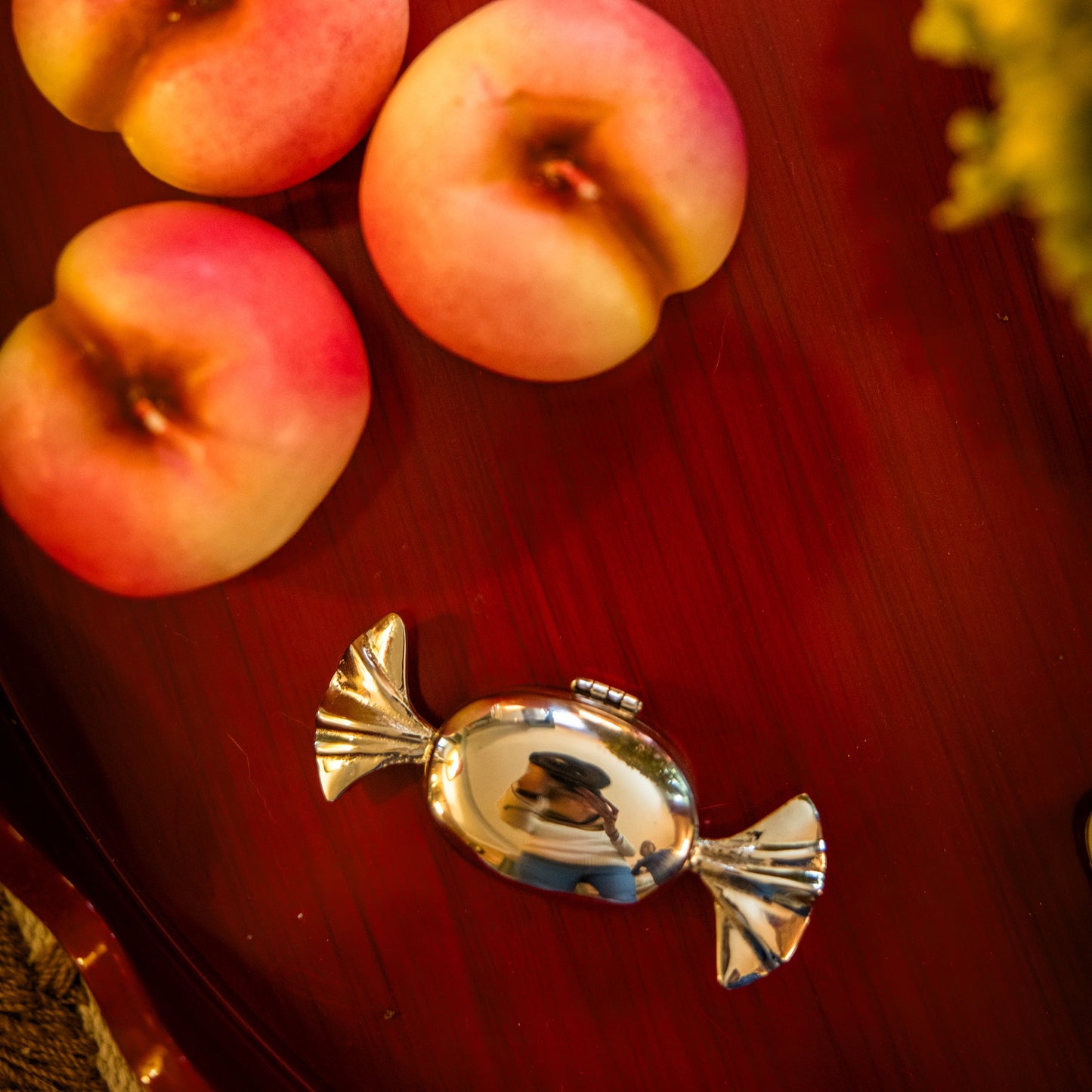 Nectarine shaped candles, and a small chrome candy shaped storage container on a red wood side table.