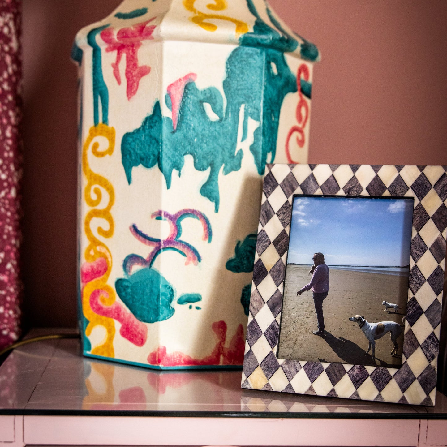 Decorative vase with colorful patterns next to a framed photo on a shelf.