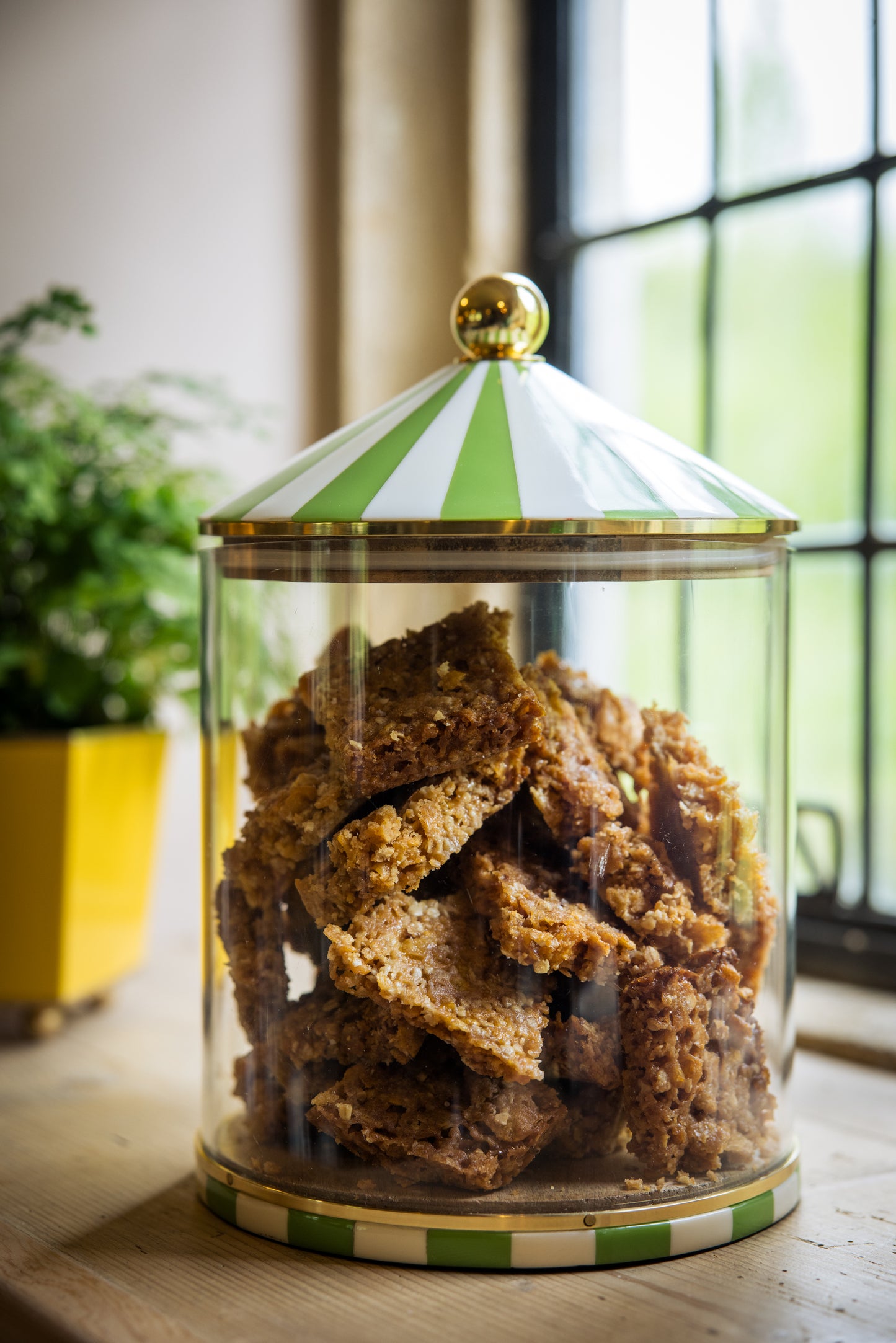 Glass jar with a green and white striped lid containing flapjack cookies on a wooden surface.