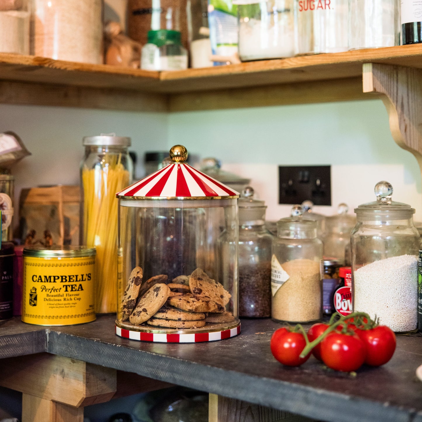 Pantry shelves with various jars and containers filled with food items in a kitchen setting the focus is on a red and white circus stripe cookie jar.