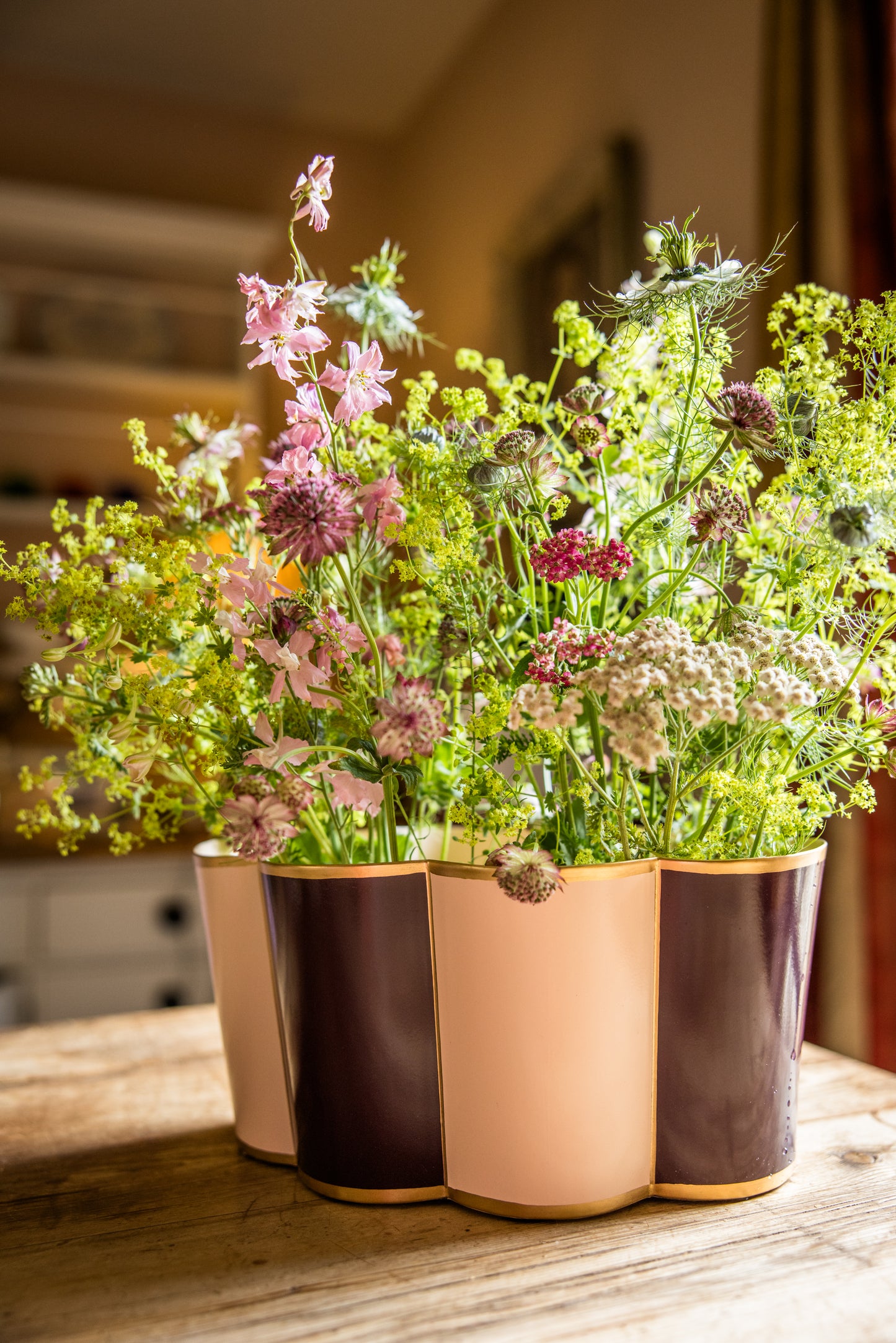 Large plant pot vase with flowers arrangement on a wooden kitchen table.