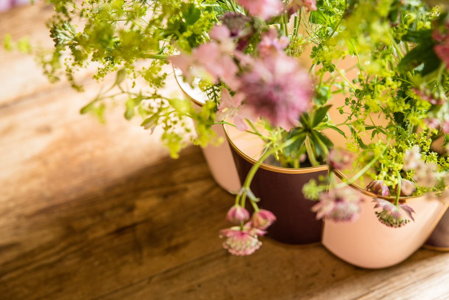 Large scalloped metal plant pot seen from above with pink flowers in the foreground on a wooden surface.