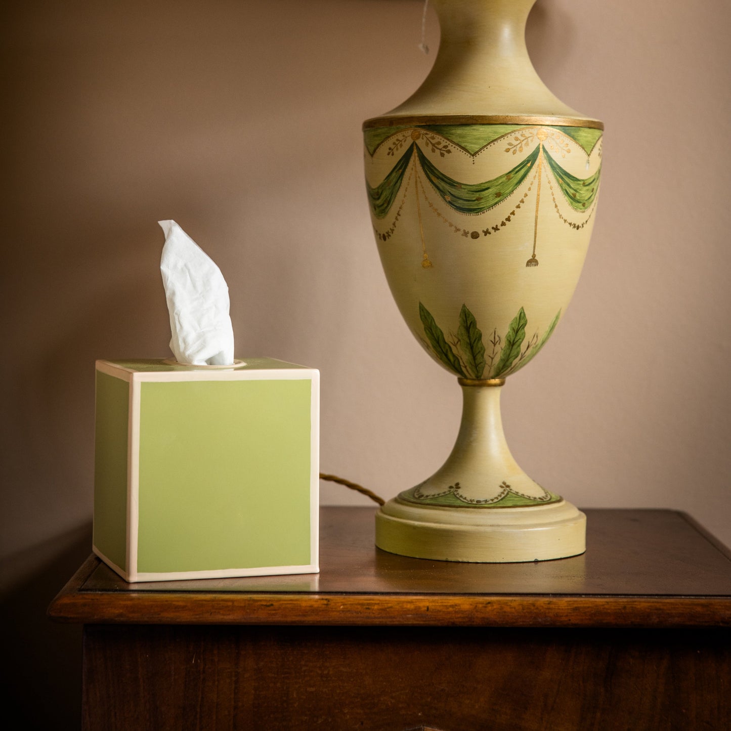 Decorative green lamp base with a matching tissue box on a wooden bedside table.