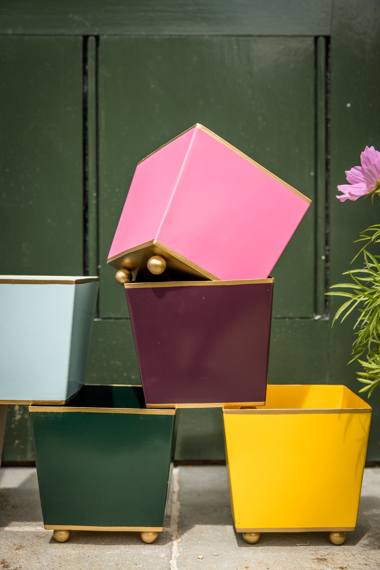 Colourful cube planters stacked on top of each other with gold bases and ball feet against a dark green background.