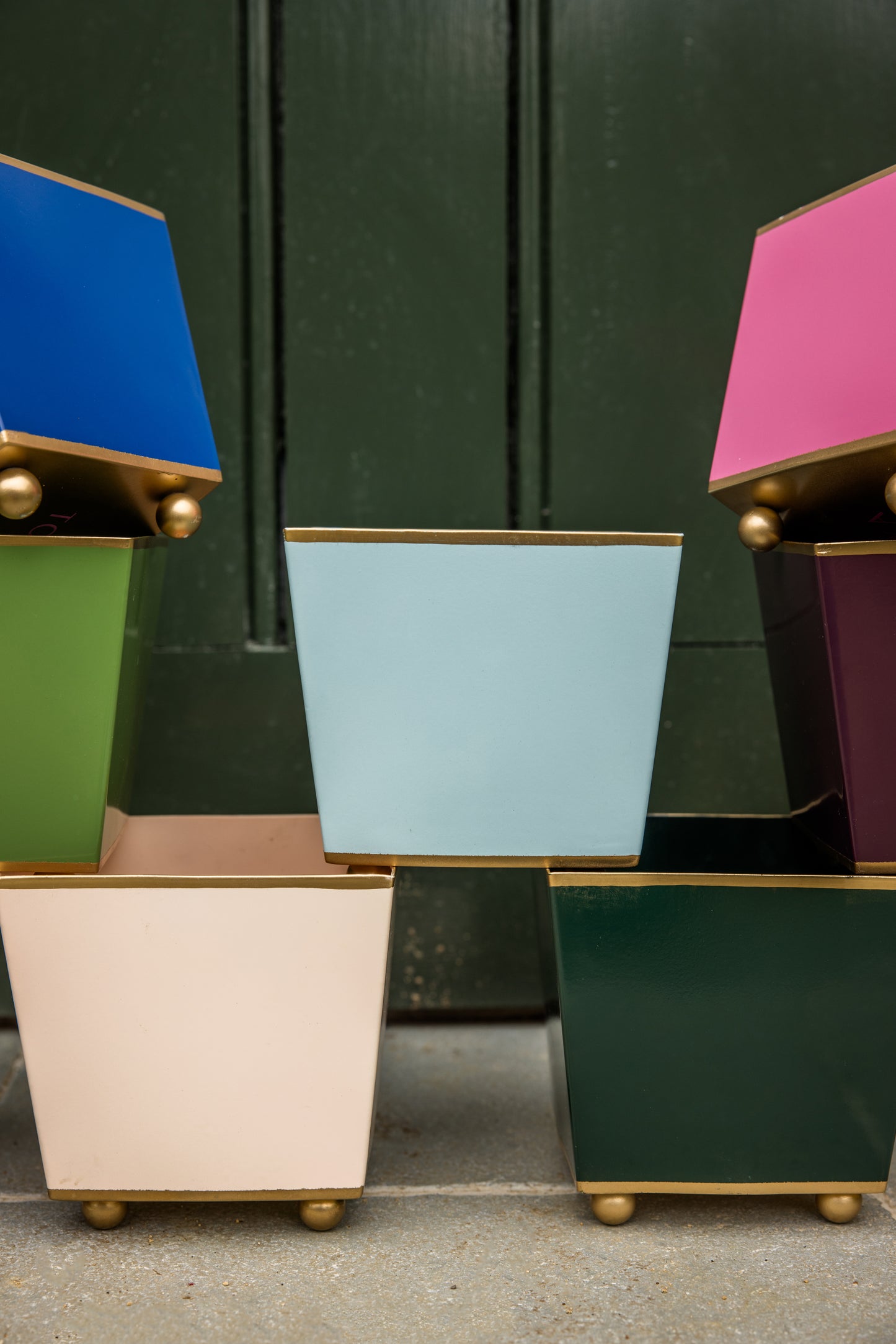 Colourful cube planters stacked on top of each other with gold bases and ball feet against a dark green background.