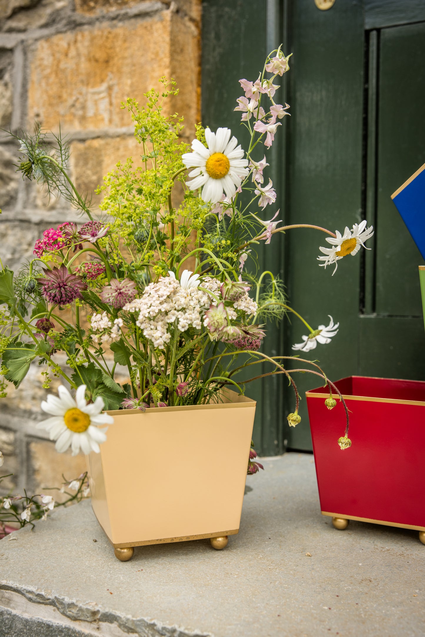 Floral arrangement in a small tan camel coloured metal planter with an empty red one in the background.
