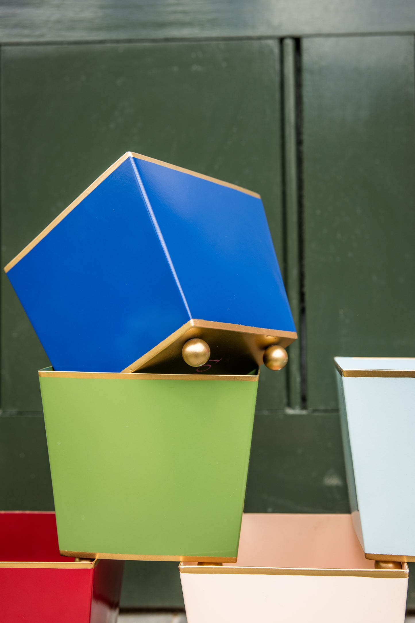 Colourful cube planters stacked on top of each other with gold bases and ball feet against a dark green background.