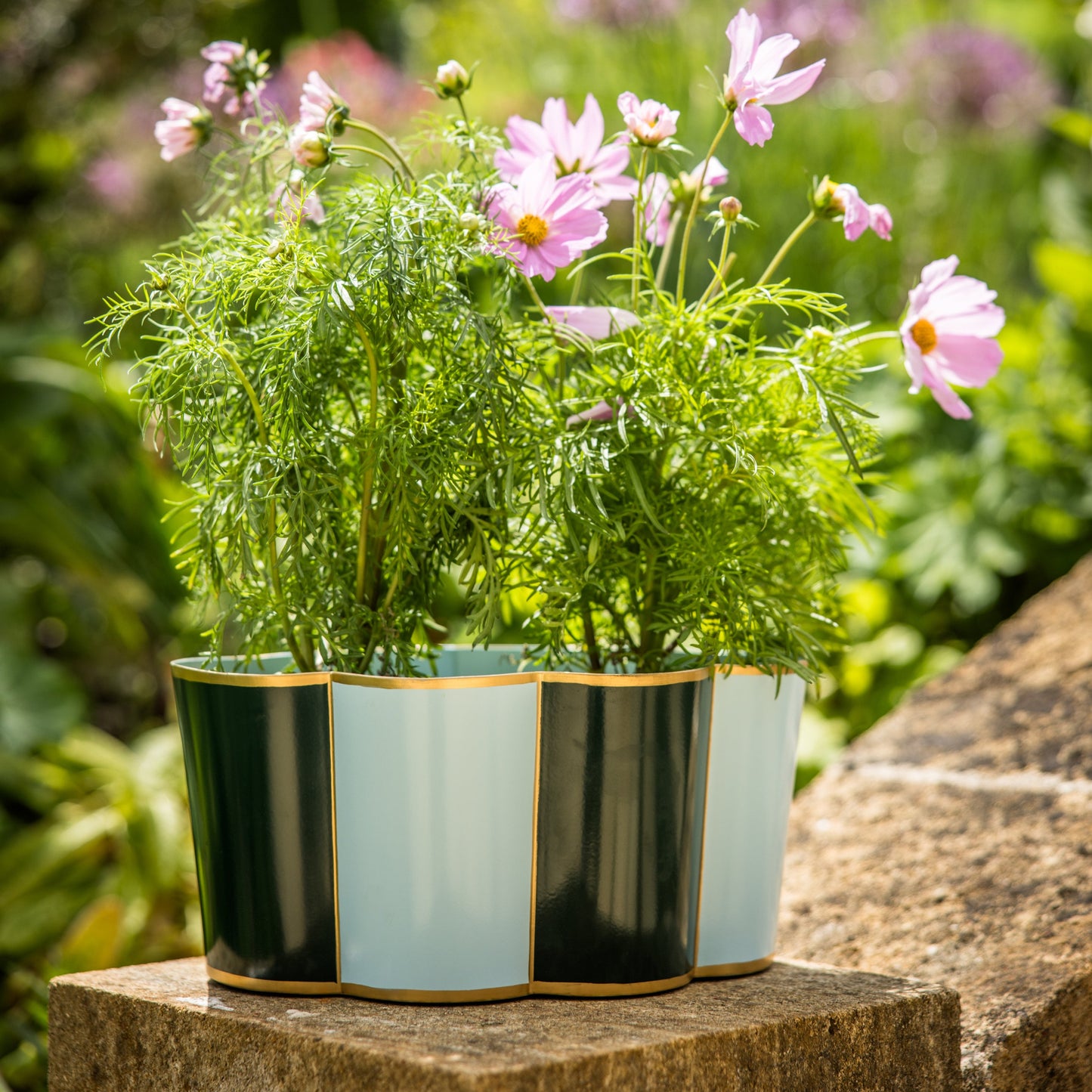 Decorative large toleware outdoor planter with pink flowers on a stone garden wall.
