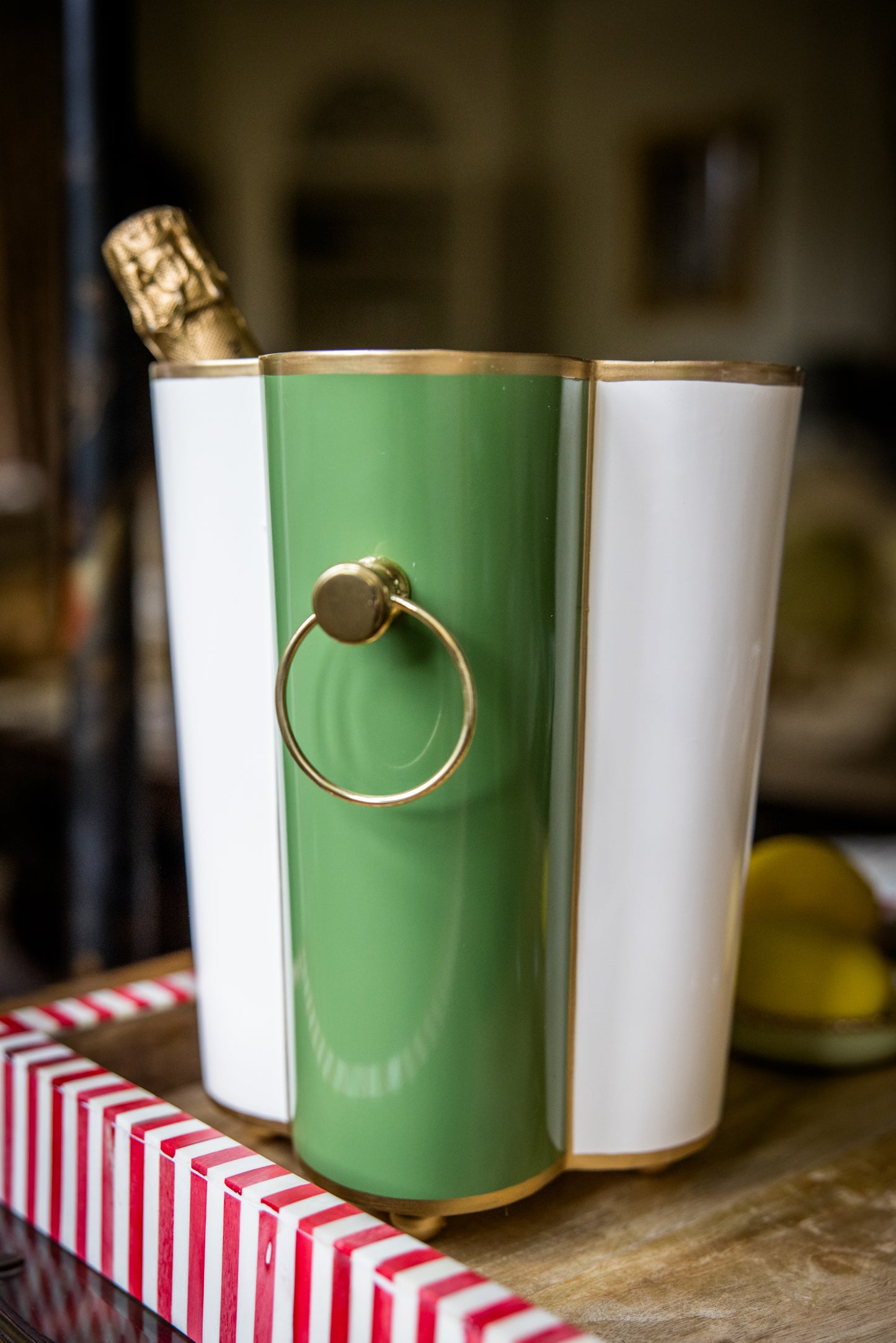 Two-toned sculptural ice bucket with a gold ring holder on the outside and a champagne bottle inside, on a wooden tray.