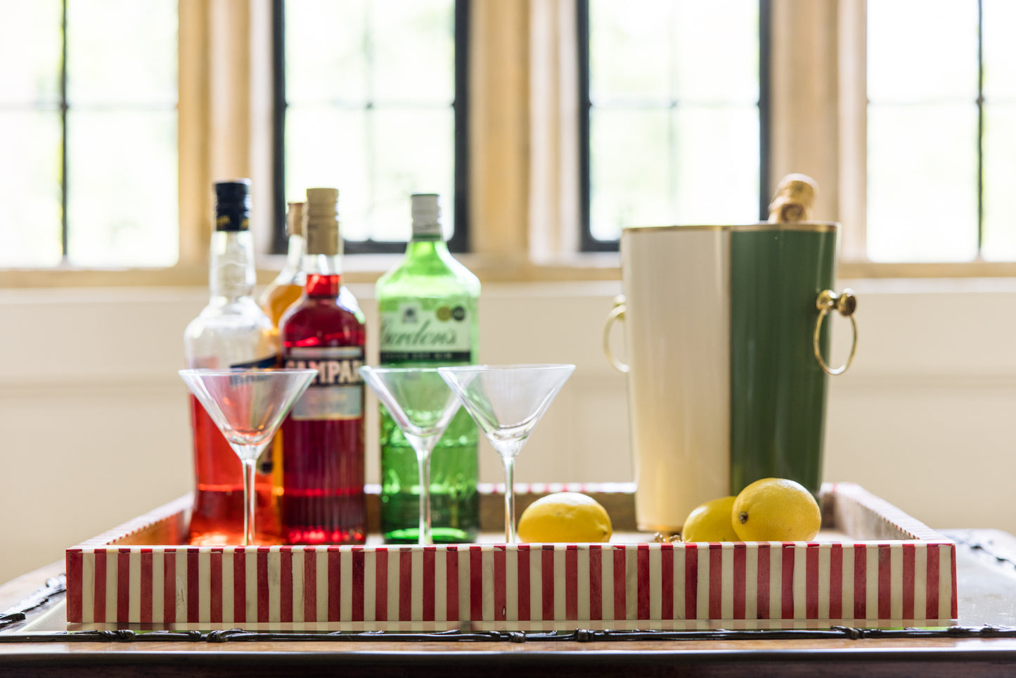 Bar cart with bottles, martini glasses an ice bucket bottle cooler and lemons on a striped tray.