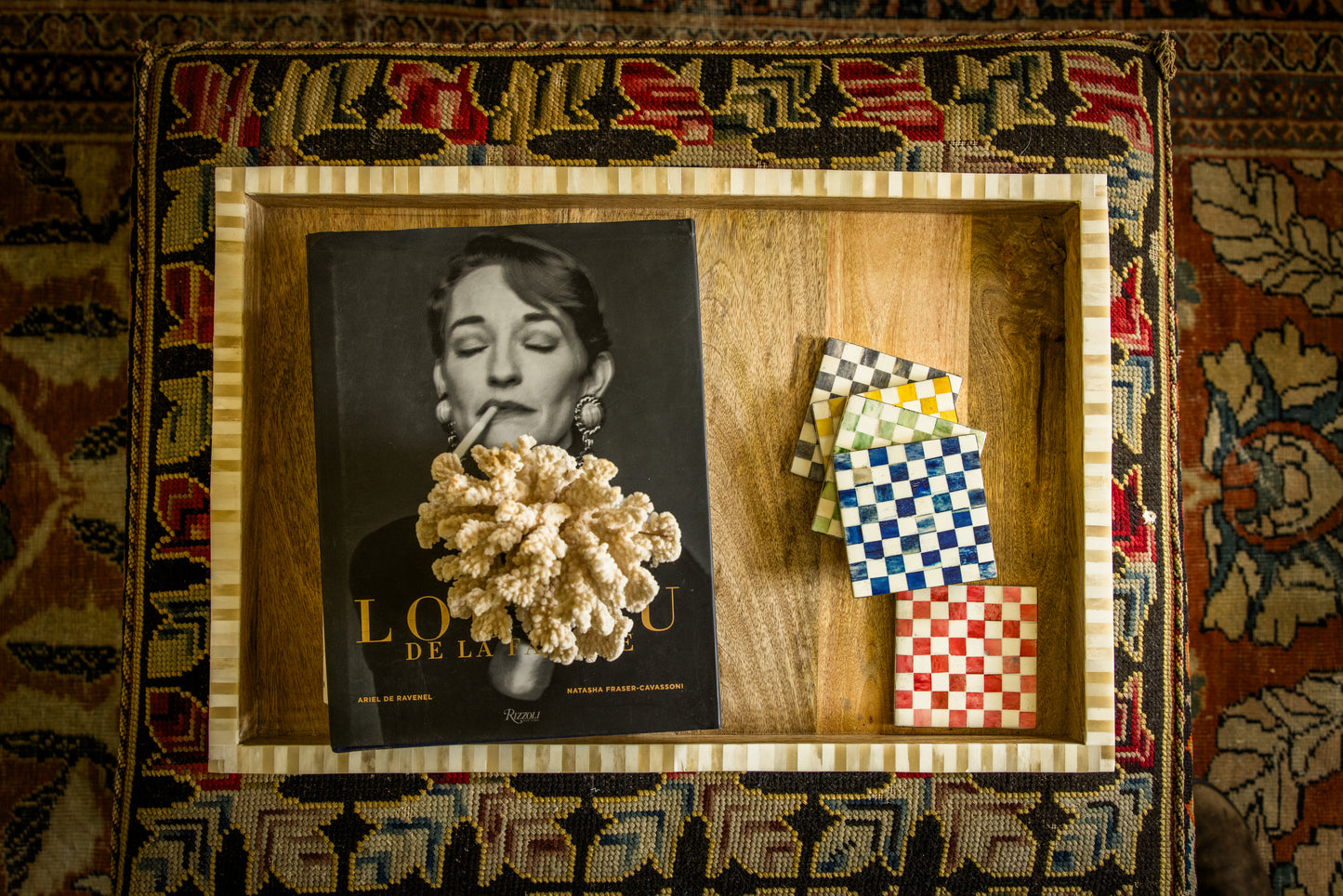 Overhead living room patterned ottoman decorative tray with a coffee table book under a piece of coral and a set of checkered coasters.