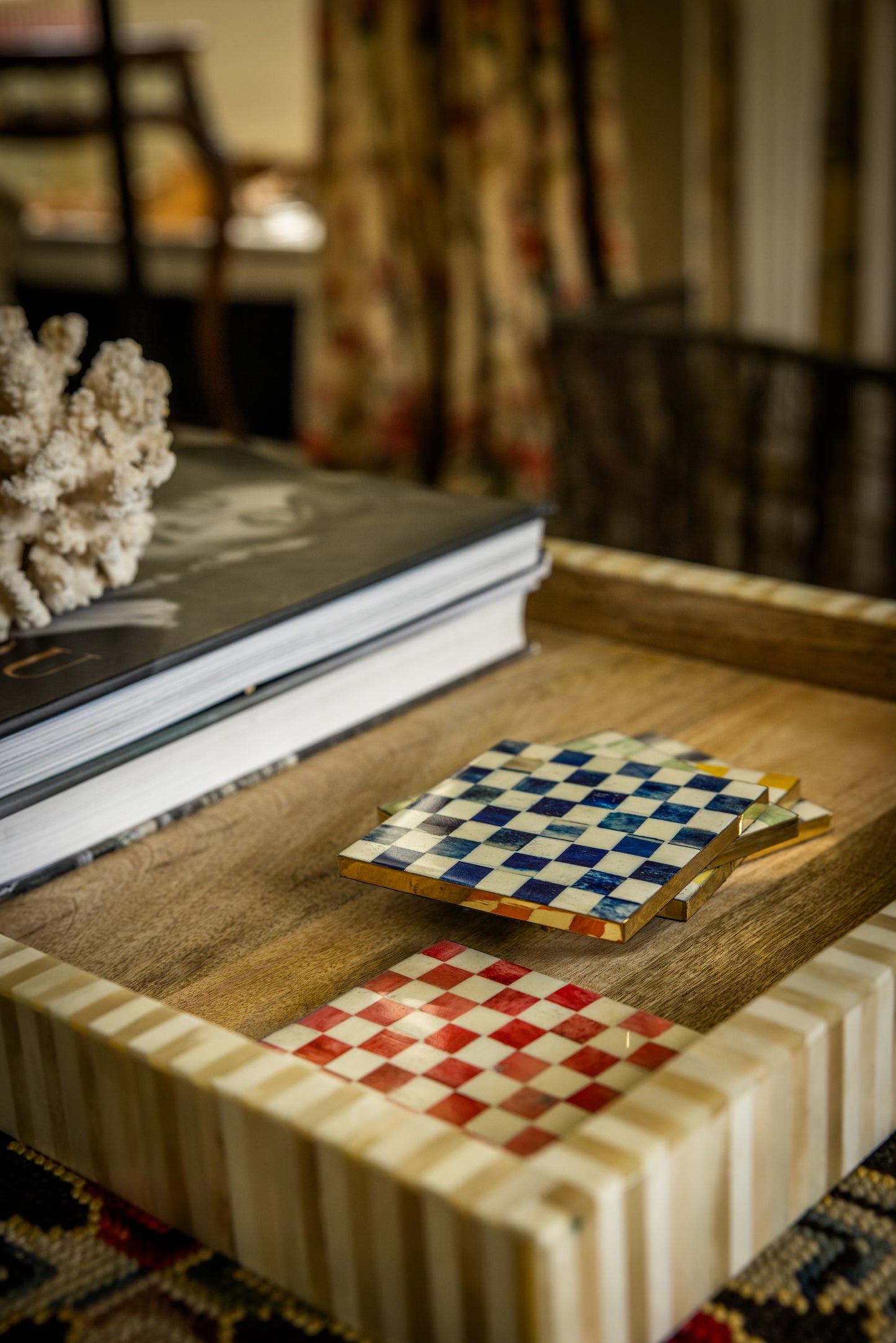 Wooden tray with checkered coasters on a coffee table with books and decorative items.