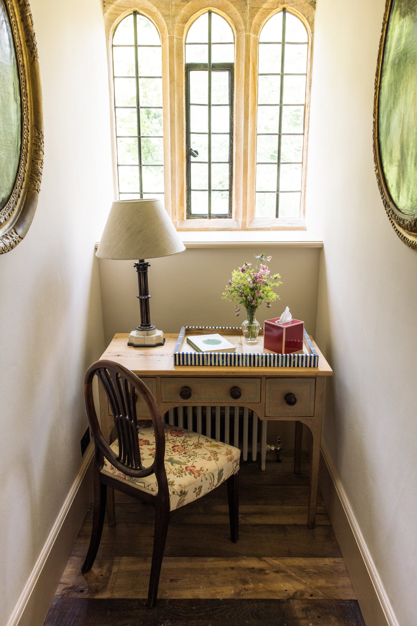 Small desk with chair under a window in a narrow room with decorative elements including a tissue box and tray.