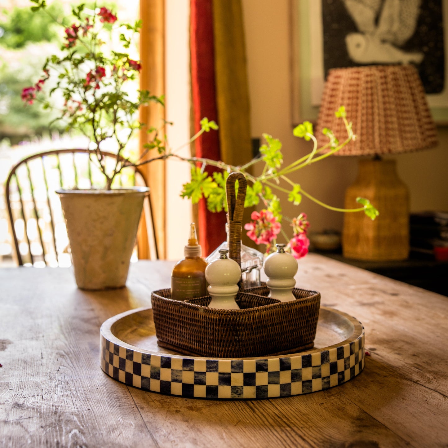 Kitchen table with decorative tray holding a condiment caddy. in the background is  a lamp, painting, curtain and garden door.