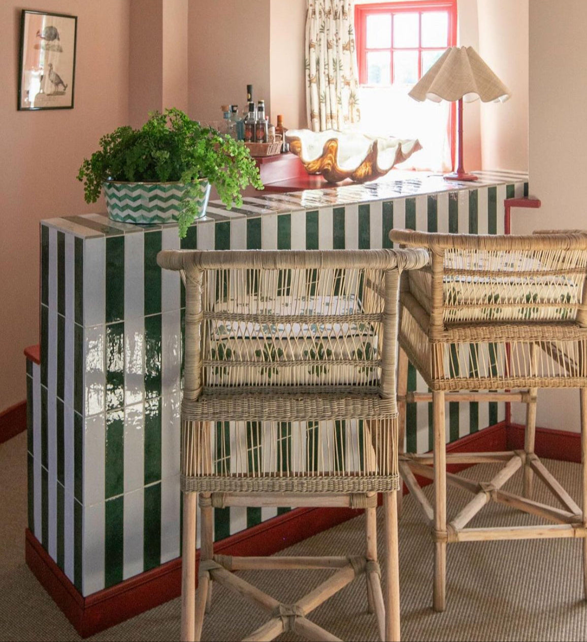 A green and white metro tile home bar with zigzag planter and fern on top along with decorative clam, drink bottles, ruffle lampshade and rattan bar stool chairs.