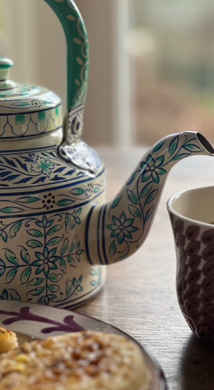 A close up of a white, blue and turquoise floral patterned teapot stove kettle showing the details of the spout, handle and lid.