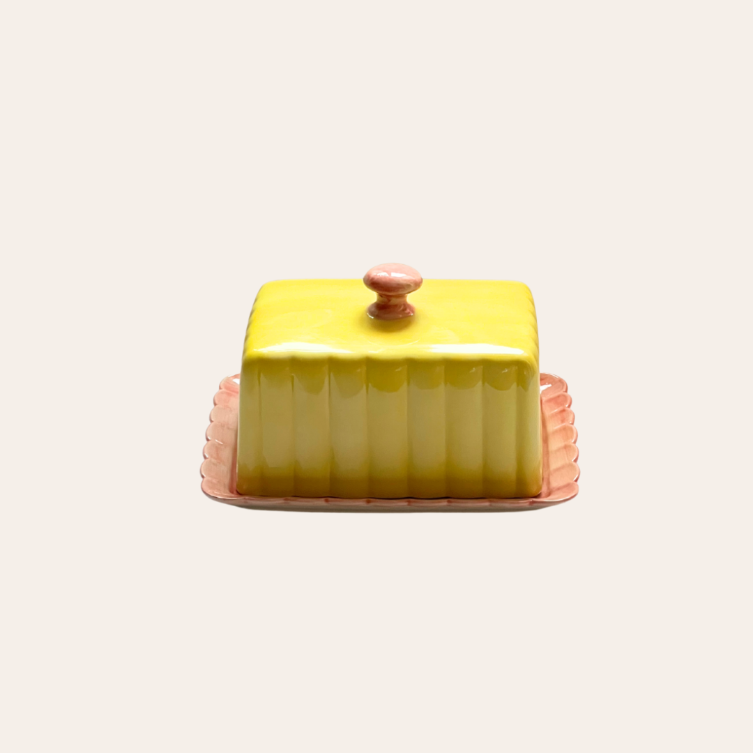 Yellow ceramic butter dish with a pink base on a light beige background