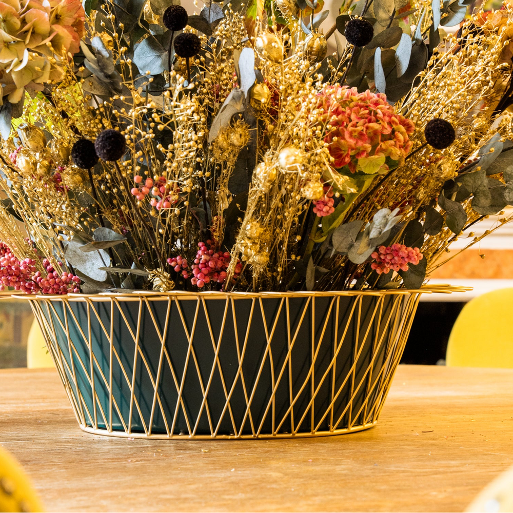 Decorative floral arrangement in a black and gold container on a table with yellow chairs.