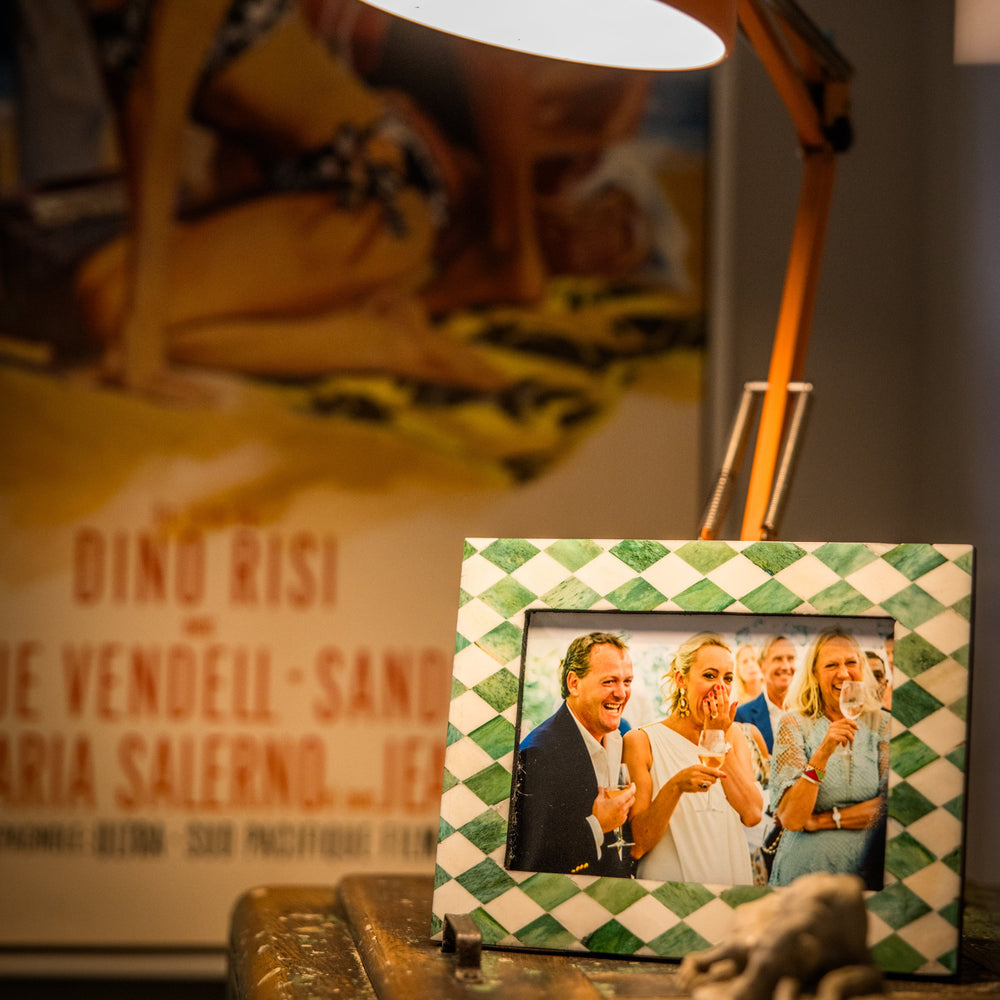 Lampshade with a photo frame featuring a couple on a table, with a blurred poster in the background.