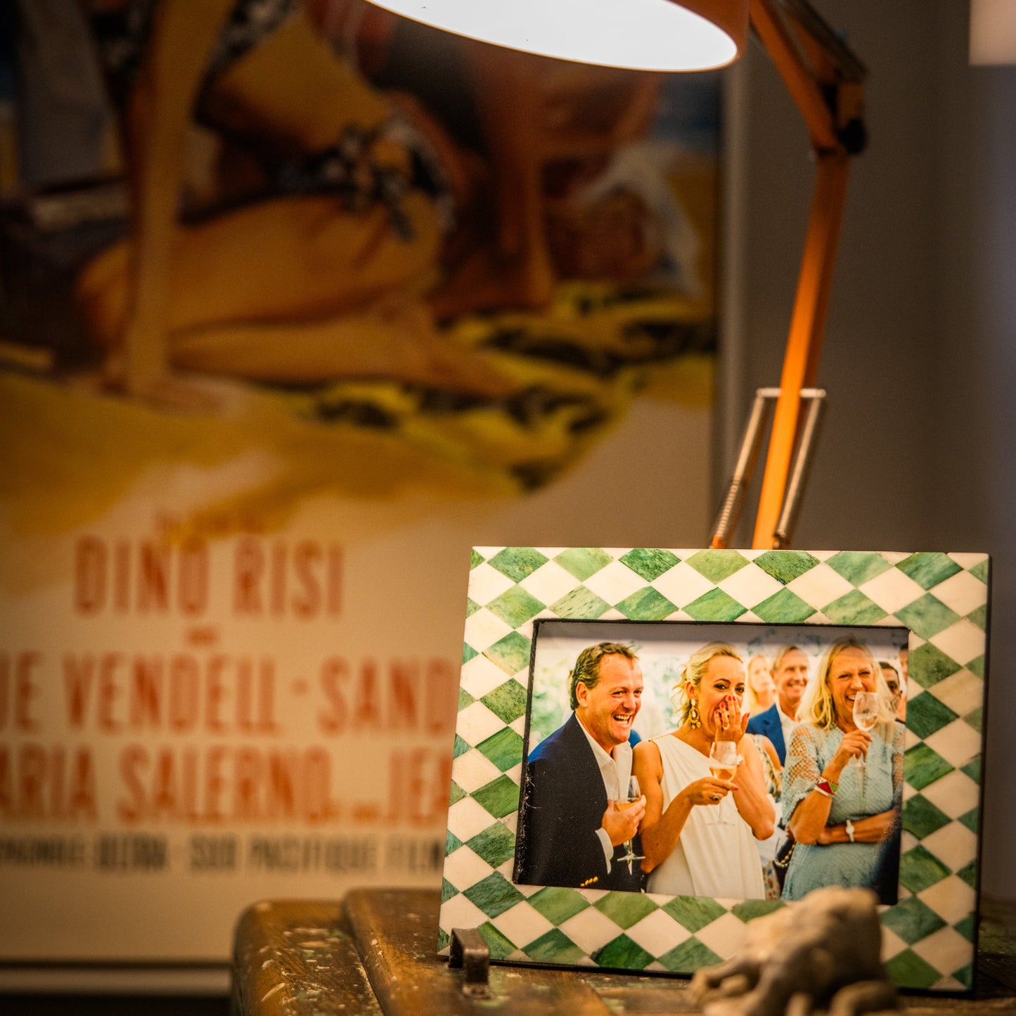 Lampshade with a photo frame featuring a couple on a table, with a blurred poster in the background.