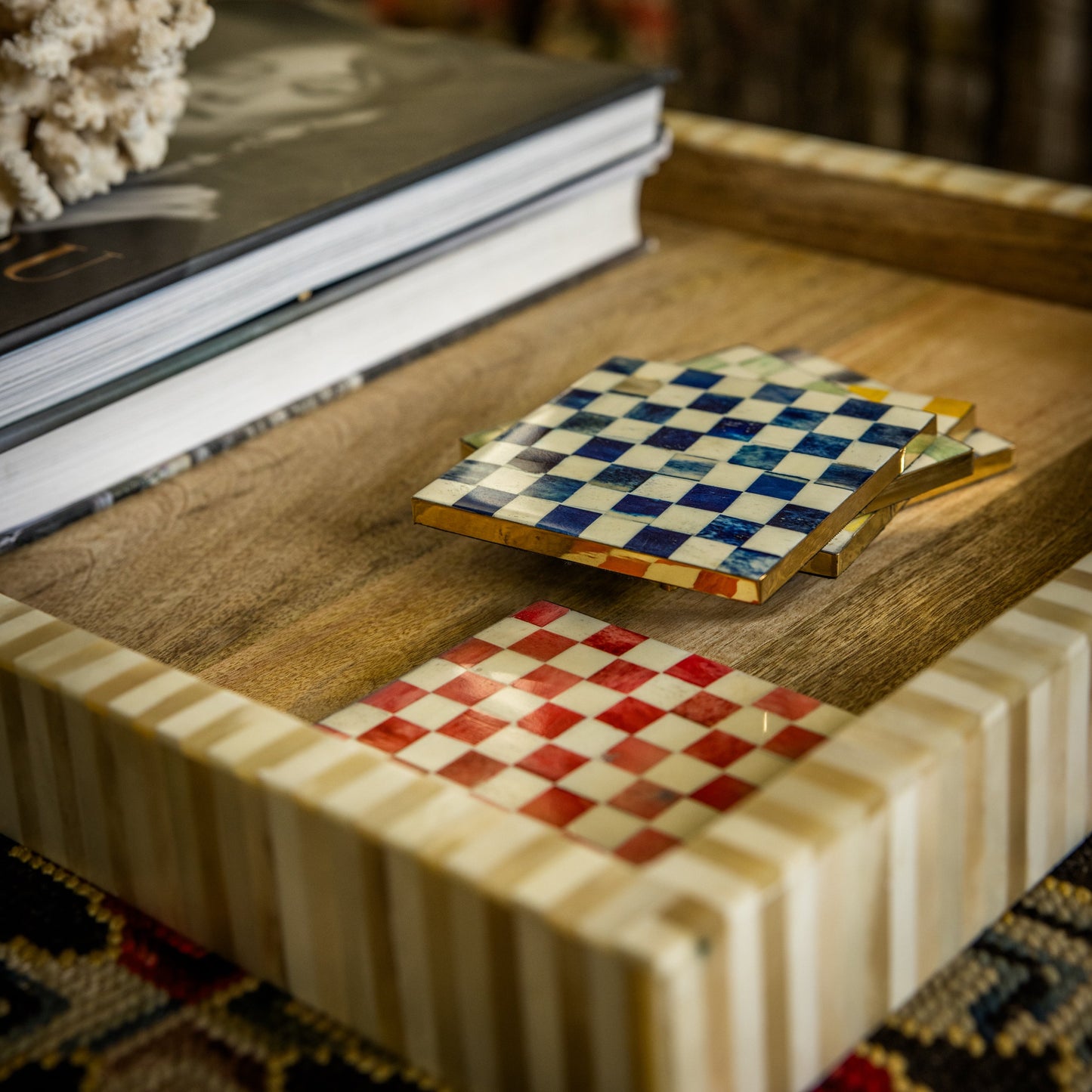 Two checkered coasters on a wooden surface with books in the background