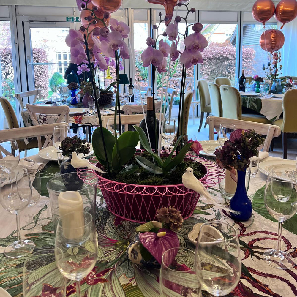 
                  
                    Decorated table with balloons and floral arrangements in a room with large windows.
                  
                