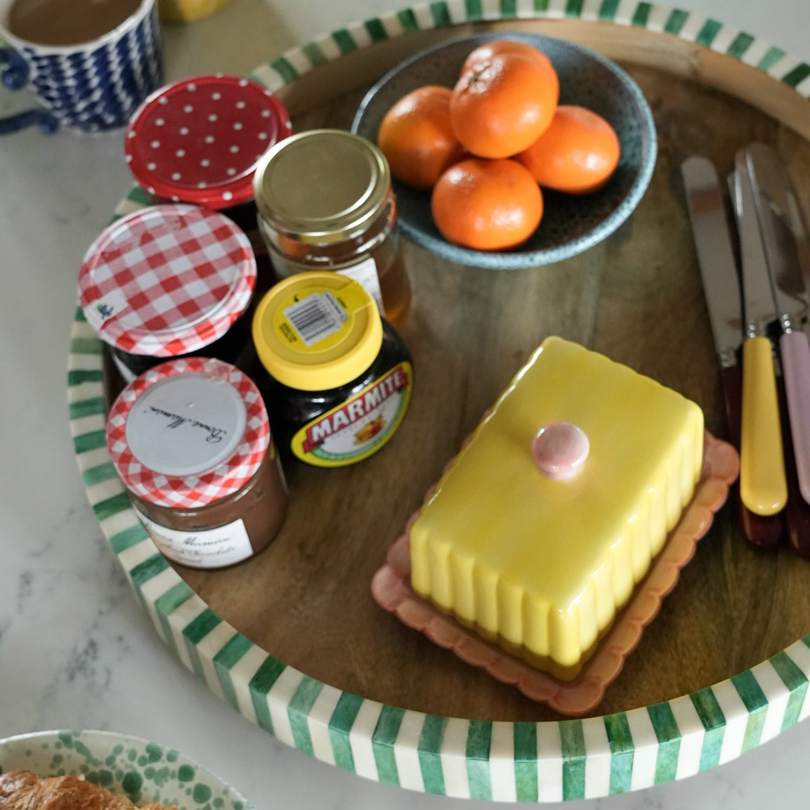 Table setting with jam jars, a cake, and fruit on a checkered tray.