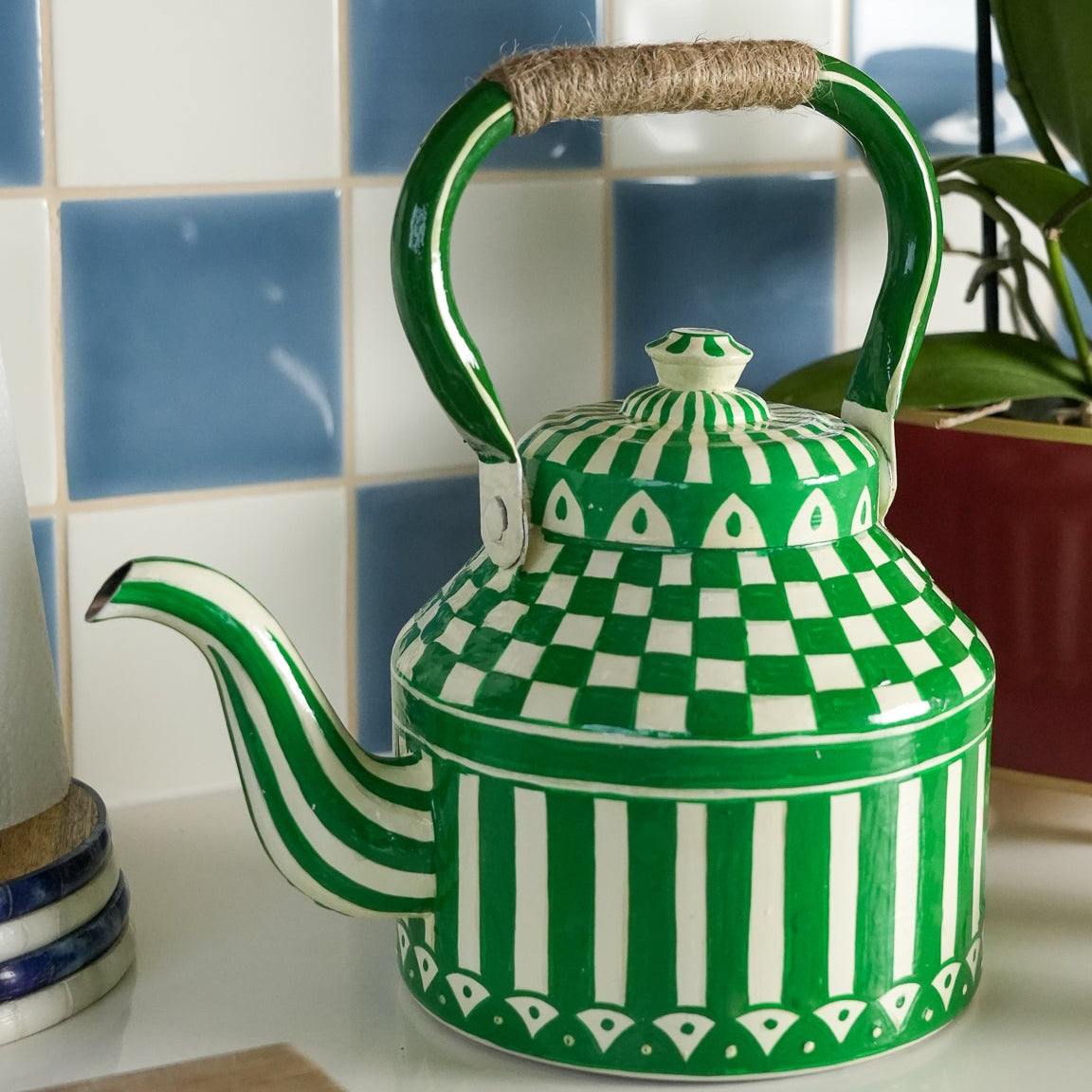 Green and white patterned teapot on a kitchen counter with a tiled wall in the background.
