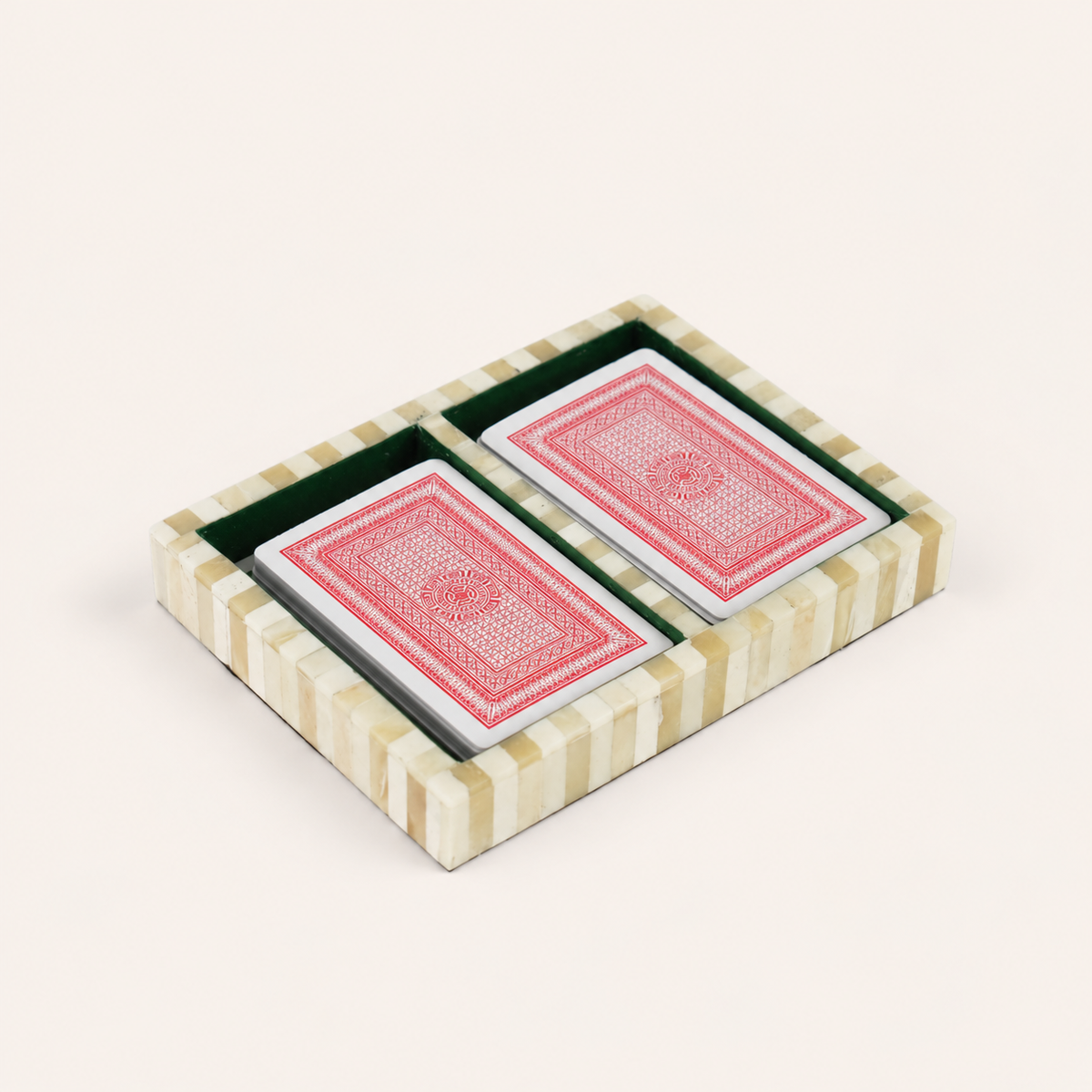 A small striped presentation box with two green-lined compartments holding two playing cards with red back designs, photographed on a plain light beige background.