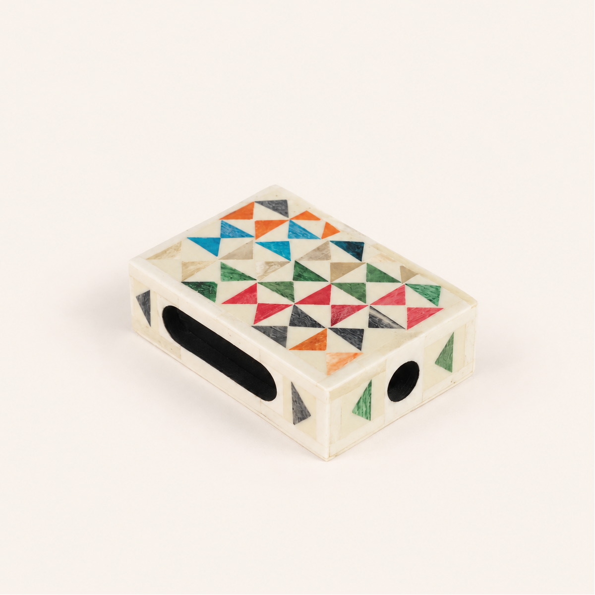 A small rectangular cream-colored case with a colorful geometric triangle inlay pattern on top, featuring a black oval cutout on one side and a circular cutout on the other, set against a plain off-white background.