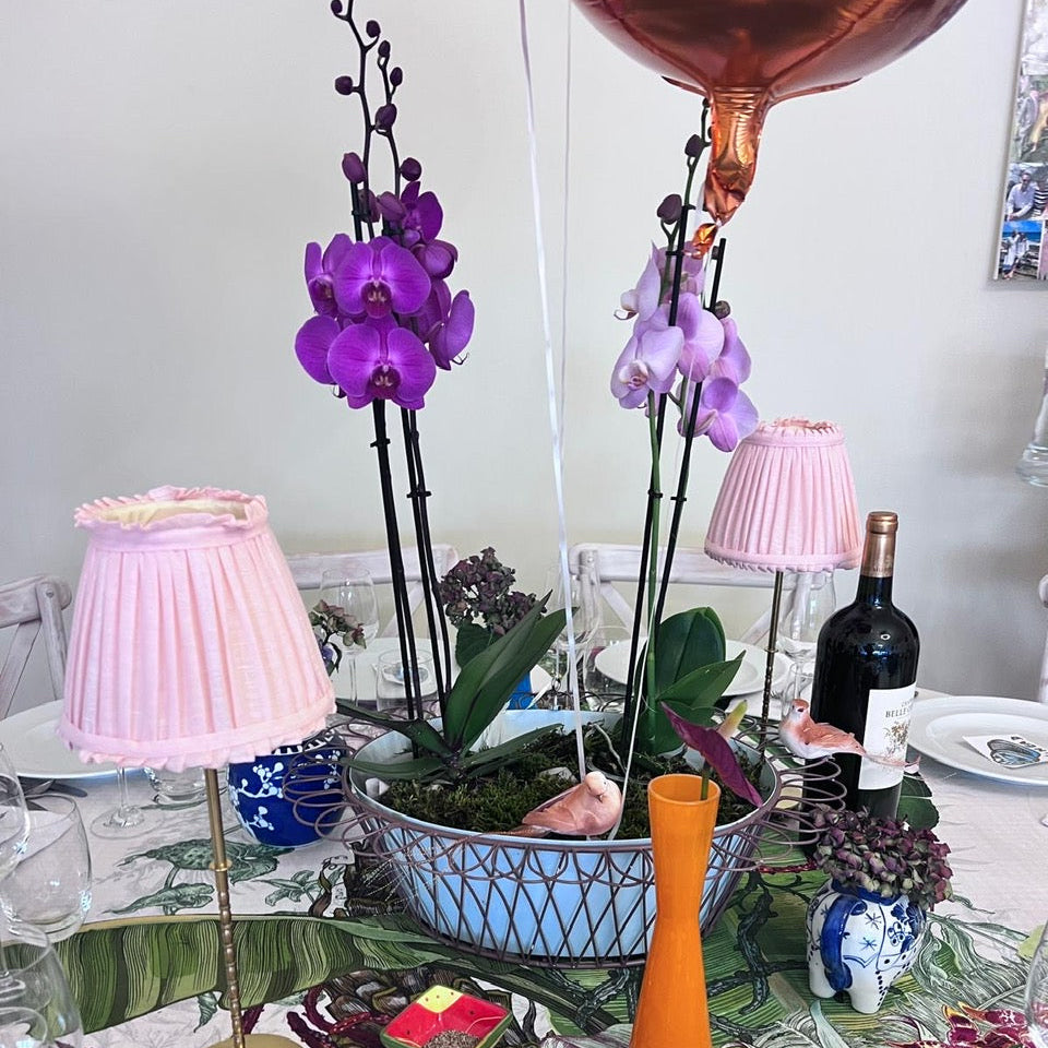 Decorative table setting with purple orchids, pink lamps, and a bottle of wine.